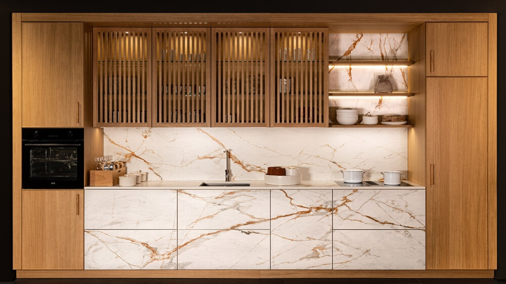 Sachsenküchen Kara kitchen range with Dekton surfaces and book-matched veining on cabinetry and wall panels.